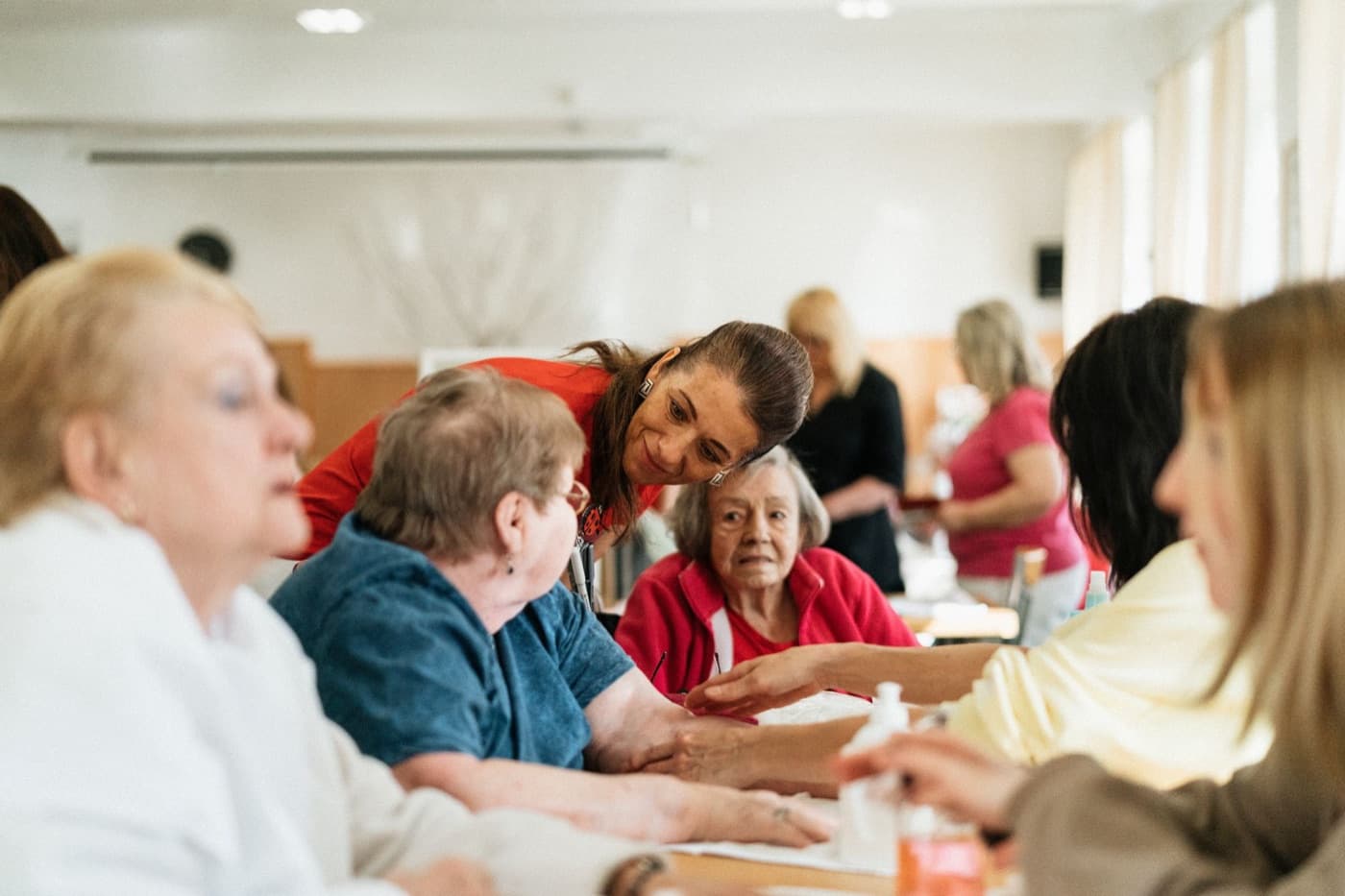 A staff member leaning in among a group of older people around a shared activity table.